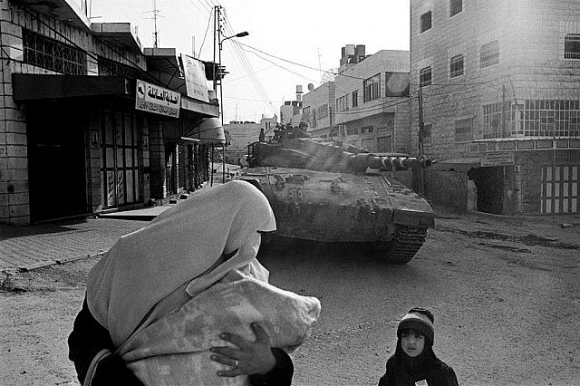 A religious Muslim woman and her children navigate their way around an Israeli tank during the Army's invasion of Hebron to help to enforce a 24-hour curfew on the city centre in February 2003 (photo: Larry Towell / Magnum)
