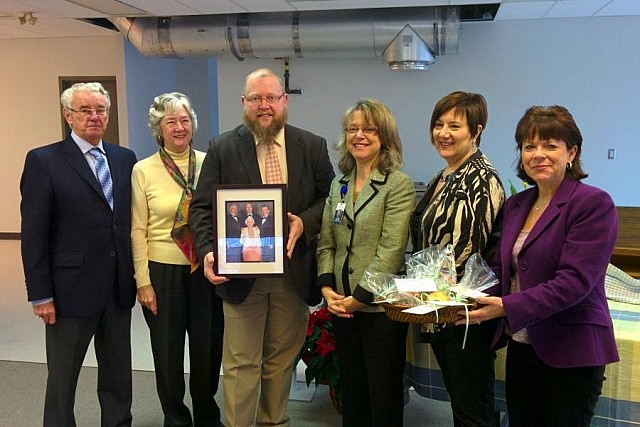 Myrtle Smith's son Hugh, daughter-in-law Ruth, grandson Todd (holding a photo of Myrtle Smith with her three sons), Dr. Rosana Salvaterra (Medical Officer of Health), Kerri Davies (member of the Peterborough County-City Board of Health Manager of Development for the Peterborough branch of the Canadian Mental Health Association), and Lesley Parnell (Peterborough city councillor and Chair of the Peterborough County-City Board of Health), holding a plate of apple muffins that Dr. Salvaterra baked using one of Myrtle Smith's recipes.